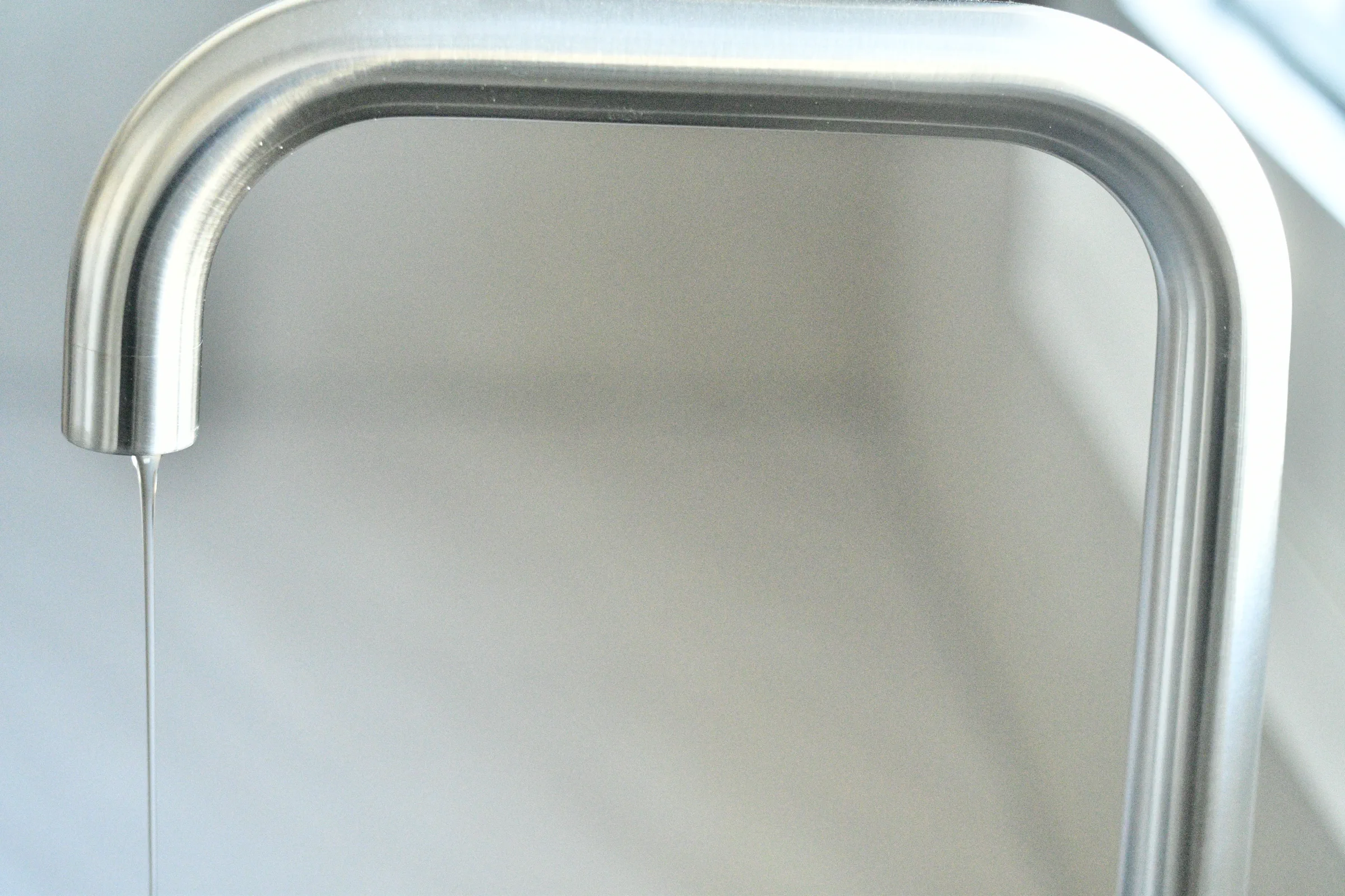 Κοντινή λεπτομέρεια καμπύλης inox μπαταρίας κουζίνας με λεπτή ροή νερού.