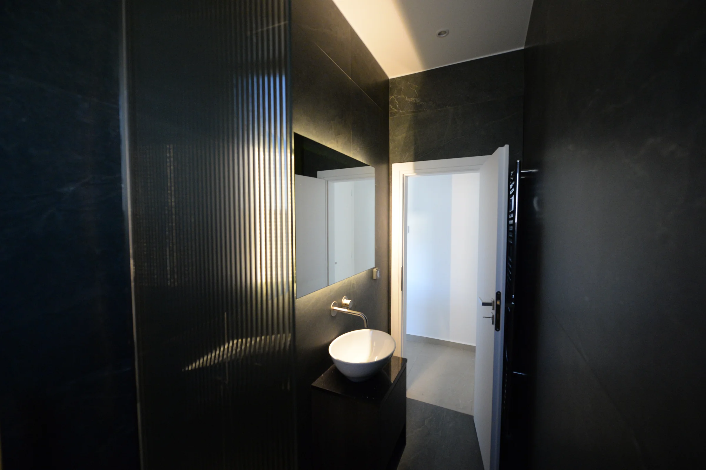 Ανακαίνιση WC στο Χαλάνδρι με σκούρα πλακίδια, φωτιζόμενο ανάγλυφο καθρέφτη, επιτραπέζιο νιπτήρα και εντοιχισμένη μπαταρία.