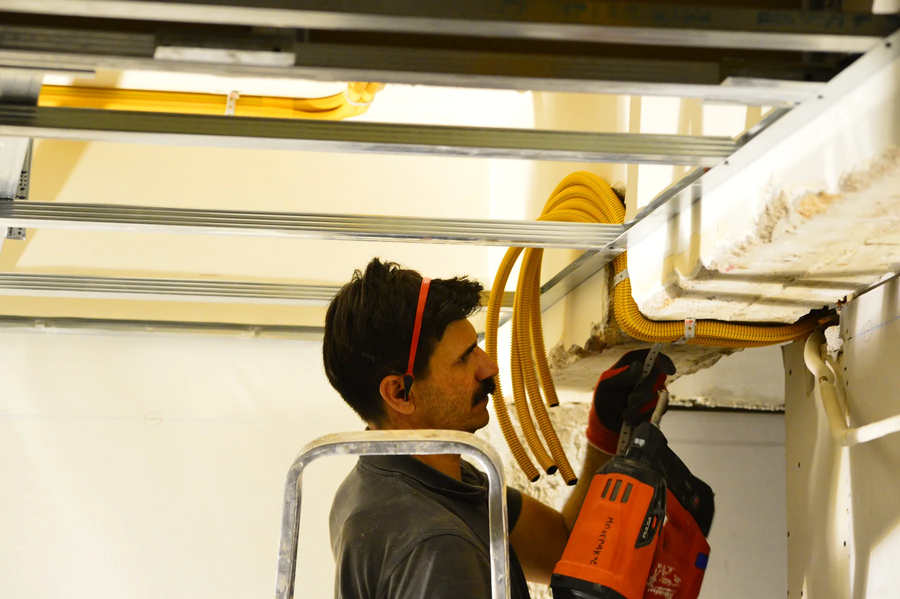 Renovator electrician using a gas-powered direct-fastening nailer for an overhead fixing during an apartment renovation in Glyfada